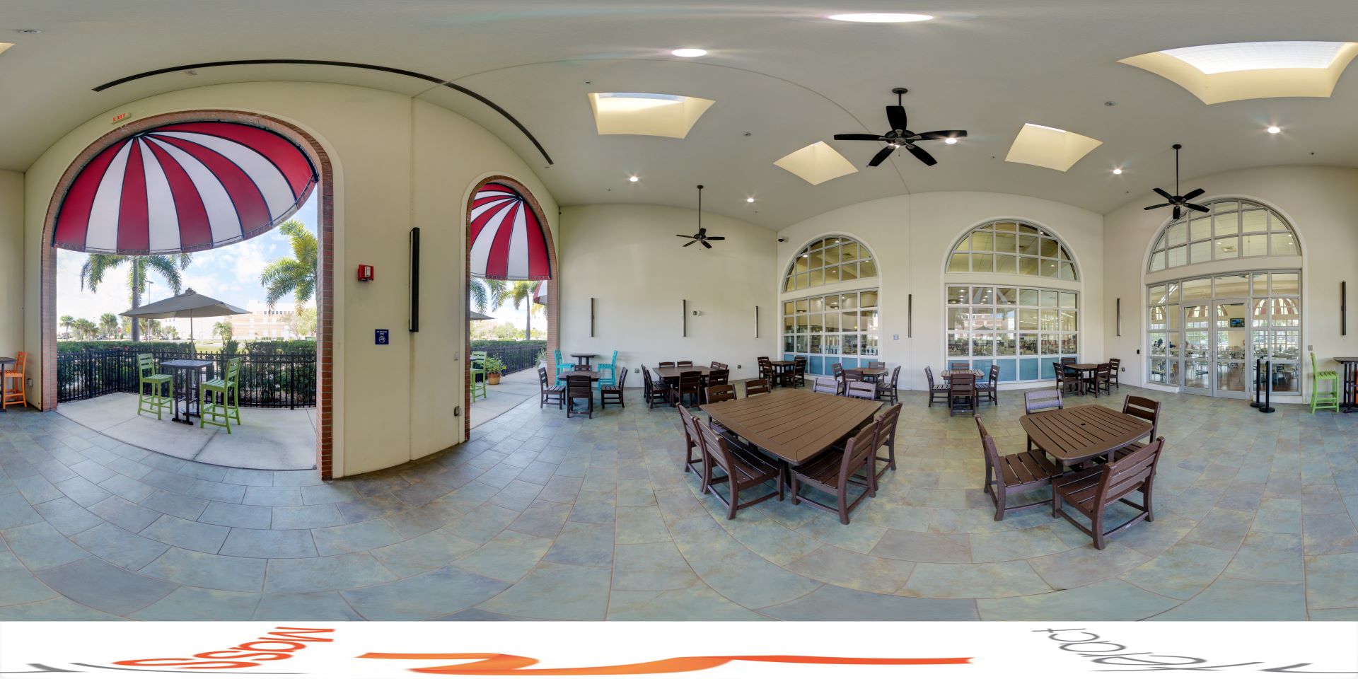 Panoramic view of a spacious outdoor patio area with various seating arrangements, ceiling fans, and large windows overlooking the dining hall interior